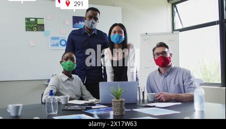 Bild von Social-Media-Ikonen über Porträt verschiedener Kollegen, die im Büro Gesichtsmasken tragen Stockfoto