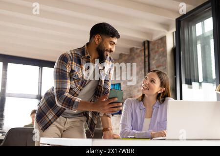 Asiatischer männlicher Profi, der in einem modernen Geschäftsbüro einer kaukasischen Kollegin ein Smartphone zeigt Stockfoto