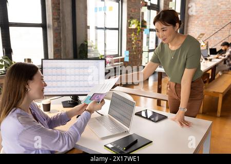 Asiatische und kaukasische Kollegen tauschen Dokumente in einem modernen Geschäftsbüro aus Stockfoto