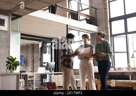 Ein vielseitiges Team diskutiert über Dokumente und steht in einem modernen Geschäftsbüro Stockfoto