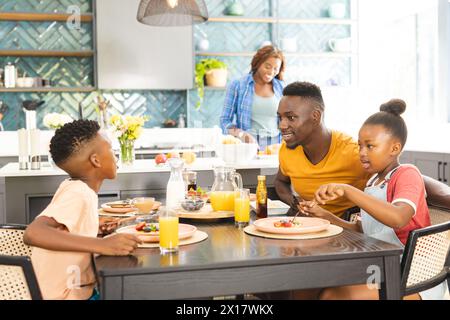 Afroamerikanische Familie genießt Frühstück zu Hause, junge Frau serviert Essen Stockfoto