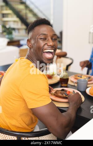 Afroamerikaner lacht beim Familienfrühstück zu Hause, Frau greift nach Essen Stockfoto