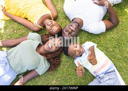 Afroamerikanische Familie liegt auf Gras, lächelt in die Kamera, zeigt Daumen hoch Stockfoto