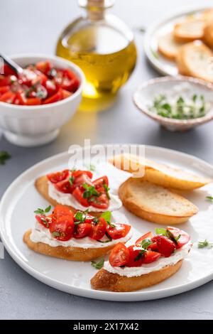 Zubereitung von Tomaten-Basilikum-Crostini oder Bruschetta mit geröstetem Baguette und Frischkäse Stockfoto