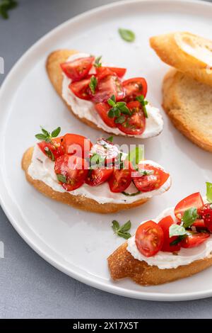 Zubereitung von Tomaten-Basilikum-Crostini oder Bruschetta mit geröstetem Baguette und Frischkäse Stockfoto