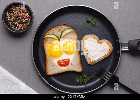 Herzförmige Spiegeleier mit Toast in der Pfanne auf grauem Tisch, Blick von oben Stockfoto
