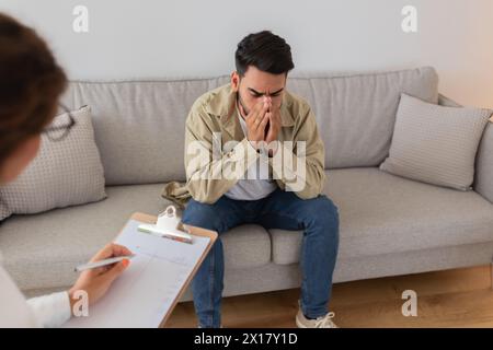 Verärgerter Mann, der während der Therapie das Gesicht versteckt, sich niederfühlt Stockfoto