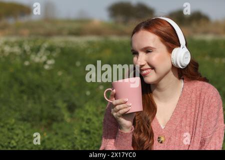Eine Frau mit langen Haaren genießt eine Tasse Kaffee, während sie mit ihren weißen kabellosen Kopfhörern Musik hört Stockfoto