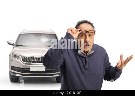 Schockierter reifer Mann vor einem Fahrzeug mit gebrochener Windschutzscheibe isoliert auf weißem Hintergrund Stockfoto