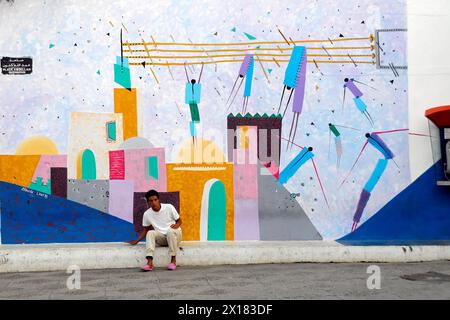 Asilah, Ein Mann sitzt entspannt vor einem farbenfrohen abstrakten Wandgemälde, Rabat, Marokko, Nordafrika Stockfoto