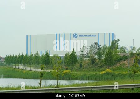 Waregem, Belgien - 22. Mai 2023: Eine Danone-Produktionsanlage ist von einem Gewässer aus zu sehen, mit Grün im Vordergrund und einem klaren Himmel Stockfoto