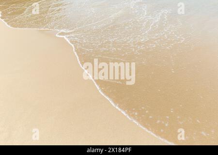 Kleine Welle an einem glatten Sandstrand an einem sonnigen Tag, von oben gesehen. Natürliche tropische Reise, Urlaub und Sommer Hintergrund mit Kopierraum. Stockfoto