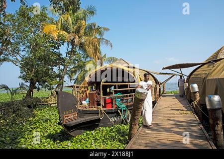 Palmen und indischer Mann mit einem Hausboot am Steg, Kanalsystem der Backwaters, Vembanad Lake, Kerala, Indien Stockfoto