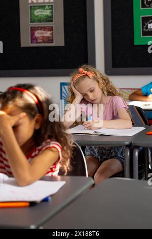 In der Schule, im Klassenzimmer, ein birassisches Mädchen und ein kaukasisches Mädchen, beide jung, konzentrieren sich auf ihre Arbeit Stockfoto