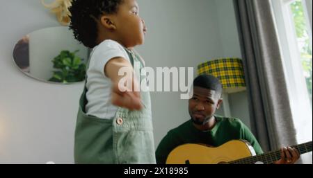 Bild von Licht, das über glücklichen afroamerikanischen Vater und Sohn blitzt, der Gitarre spielt Stockfoto