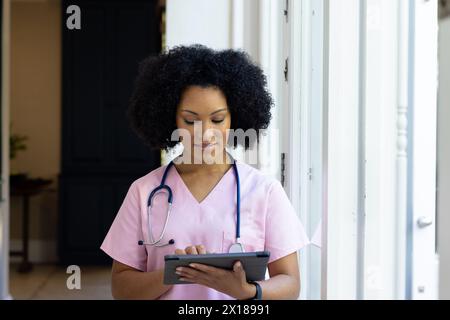 Junge birassische Krankenschwester, die rosa Peelings trägt und zu Hause die Tablette überprüft Stockfoto