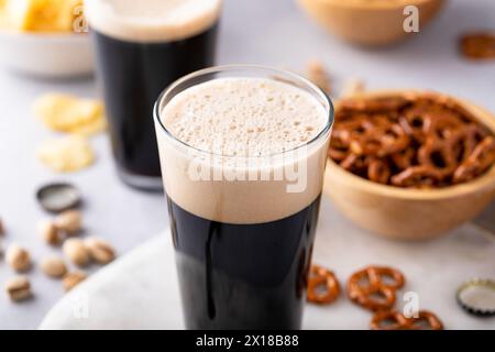 Dunkles, kräftiges Bier in hohen Gläsern mit Nüssen, Brezeln und Chips Stockfoto