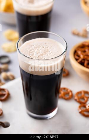 Dunkles, kräftiges Bier in hohen Gläsern mit Nüssen, Brezeln und Chips Stockfoto