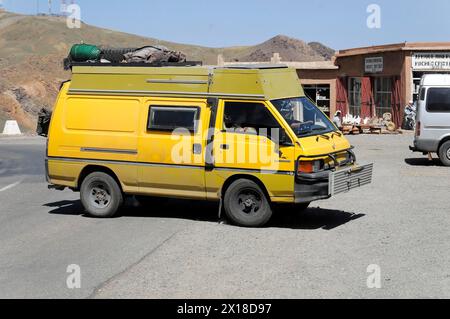 Am Tichka-Pass, Col du Tichka, 2260 m, parkte Ein gelber Van neben einem Gebäude in einer trockenen Landschaft, südlicher Hochatlas, Marokko Stockfoto