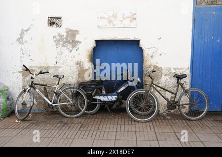 Essaouira, zwei Fahrräder, die an eine Wand neben einer blauen Tür in einer städtischen Umgebung gelehnt sind, Essaouira, Marokko Stockfoto