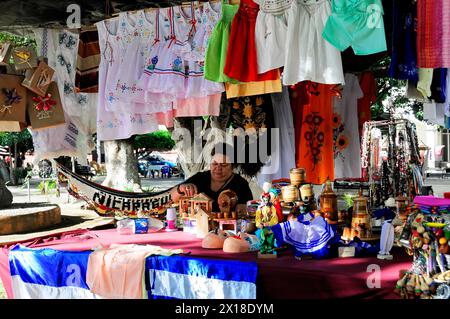 Leon, Nicaragua, Eine bunte Auswahl an Kunsthandwerk und Kleidung an einem Marktstand mit einer Verkäuferin im Hintergrund, Mittelamerika, Mittelamerika Stockfoto