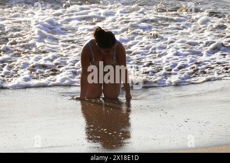 Strand in der Nähe von Poneloya, Las Penitas, Leon, Nicaragua, Eine Frau kniet am sonnigen Strand und beobachtet die Wellen, Mittelamerika, Mittelamerika Stockfoto