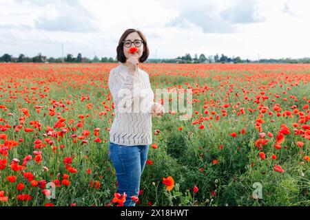 Dunkelhaarige Frau, die auf dem Mohnfeld steht und Blumen in der Hand hält Stockfoto