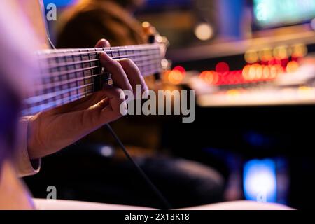 Talentierte Sängerin spielt neue Akustikgitarre im Musikstudio und nimmt neue Songs mit einem Toningenieur im Kontrollraum auf. Ein Musiker, der Songs auf dem Instrument produziert. Nahaufnahme. Stockfoto