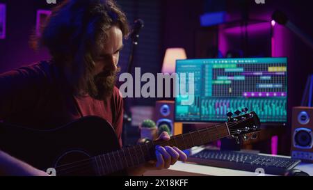 Junger Mann, der Gitarre spielt und Musik mit der Equalizer daw Software-Schnittstelle kreiert. Musikproduzent nimmt im Heimstudio einen Song auf und mischt akustische Klänge auf der Stereo-Konsole. Kamera B.. Stockfoto