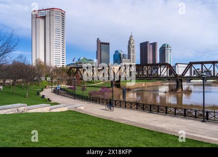 Columbus, OH - 7. April 2024: Blick auf das Finanzviertel der Innenstadt vom Fluss Scioto durch eine Eisenbahnfachwerkbrücke Stockfoto