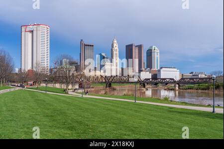 Columbus, OH - 7. April 2024: Blick auf das Finanzviertel der Innenstadt vom Fluss Scioto durch eine Eisenbahnfachwerkbrücke Stockfoto