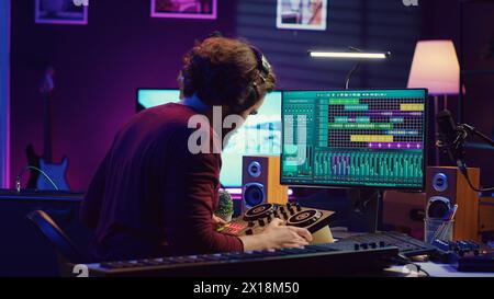 Toningenieur synchronisiert Video- und Audiospuren in seinem Heimstudio, bearbeitet Techniken auf Aufnahmen. Junger Künstler, der die Musiklautstärke nach dem Mischen und Mastering von Melodien mit dem Verstärker anpasst. Kamera A.. Stockfoto