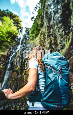 Beschreibung: Weibliche Touristen mit Rucksack lehnt sich an den Holzzaun des Aussichtspunkts und beobachtet den grünen, bewachsenen Risco-Wasserfall. 25 Fontes Waterfalls, M Stockfoto