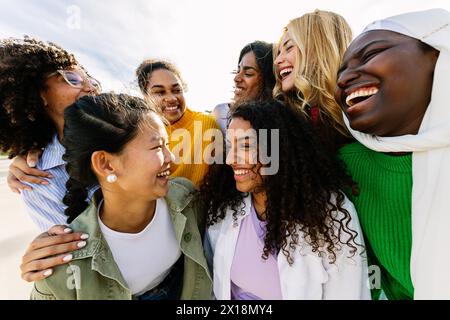 Sieben glückliche junge Erwachsene Frauen aus verschiedenen Kulturen, die gemeinsam im Freien lachen Stockfoto