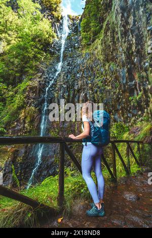 Beschreibung: Weibliche Touristen mit Rucksack lehnt sich an den Holzzaun des Aussichtspunkts und beobachtet den grünen, bewachsenen Risco-Wasserfall. 25 Fontes Waterfalls, M Stockfoto