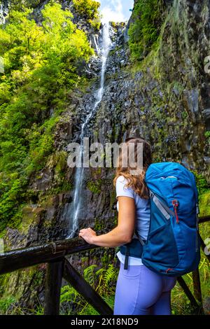 Beschreibung: Weibliche Touristen mit Rucksack lehnt sich an den Holzzaun des Aussichtspunkts und beobachtet den grünen, bewachsenen Risco-Wasserfall. 25 Fontes Waterfalls, M Stockfoto