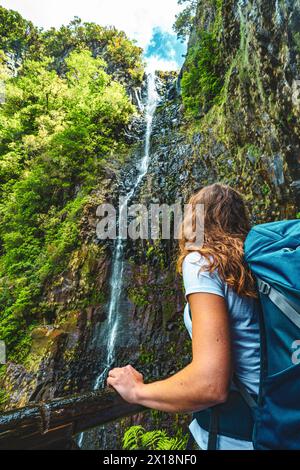 Beschreibung: Weibliche Touristen mit Rucksack lehnt sich an den Holzzaun des Aussichtspunkts und beobachtet den grünen, bewachsenen Risco-Wasserfall. 25 Fontes Waterfalls, M Stockfoto