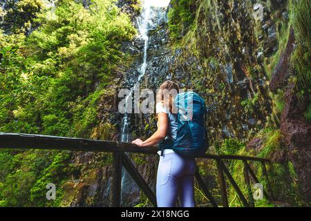 Beschreibung: Sportlicher Tourist mit Rucksack lehnt sich an den hölzernen Zaun des Aussichtspunkts und beobachtet den grün bewachsenen Risco-Wasserfall. 25 Fontes Wasserfälle, Stockfoto