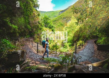 Beschreibung: Sportlicher Tourist mit Rucksack Spaziergänge entlang von Bäumen, Kanal Pfad durch an einem sonnigen Tag. 25 Fontes Wasserfälle, Madeira Island, Portu Stockfoto