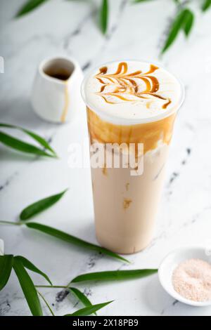 Karamell-Milch-Tee-Latte in einem hohen Glas mit Kaltschaum und mit Karamellsauce getränkt Stockfoto