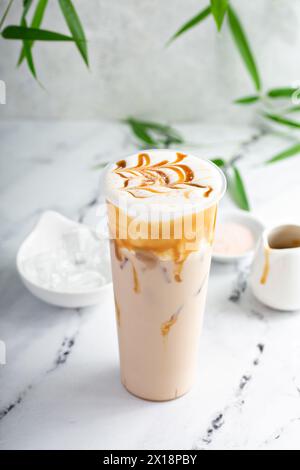 Karamell-Milch-Tee-Latte in einem hohen Glas mit Kaltschaum und mit Karamellsauce getränkt Stockfoto