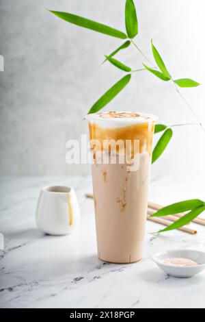 Karamell-Milch-Tee-Latte in einem hohen Glas mit Kaltschaum und mit Karamellsauce getränkt Stockfoto