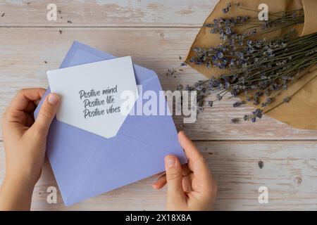 Text „POSITIVE MIND LIFE VIBES“ auf unterstützender Nachricht, die Sie auf Papier erinnern, aus violettem Umschlag. Flache Zusammensetzung trockene Lavendelblüten. Konzept von innerem Glück, Verlangsamung digitaler Detox persönliche Erfüllung. Draufsicht Stockfoto