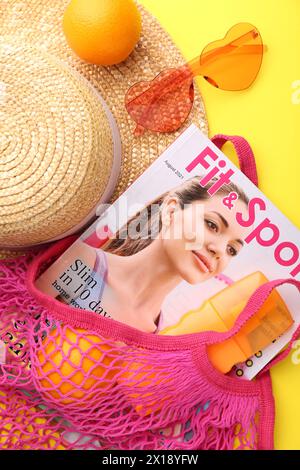 Schnur-Tasche mit frischen Orangen, Magazin und Strand-Accessoires auf gelbem Hintergrund, flacher Lay Stockfoto