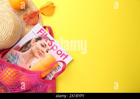 Schnur-Tasche mit frischen Orangen, Magazin und Strand-Accessoires auf gelbem Hintergrund, flacher Lay. Leerzeichen für Text Stockfoto