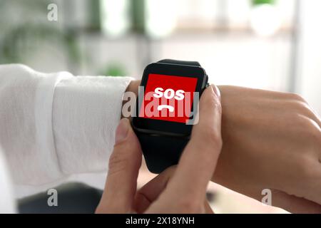 Frau mit SOS-Funktion bei Smartwatch drinnen, Nahaufnahme Stockfoto