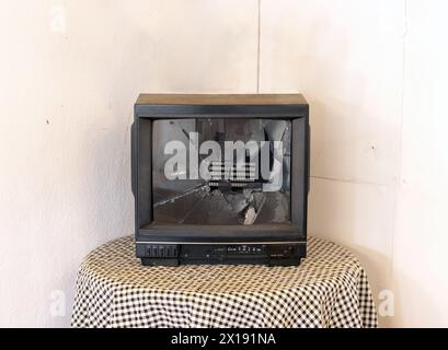 Ein kaputter Fernseher auf einem runden Tisch in der Ecke des Zimmers Stockfoto