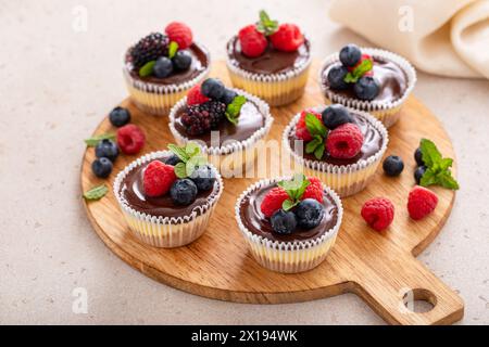 Mini-Vanillekäsekuchen in einer Muffinpfanne mit Schokoladenganache serviert mit frischen Beeren Stockfoto
