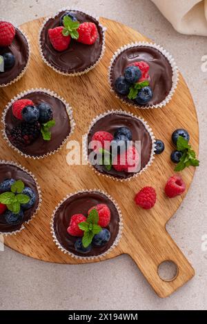Mini-Vanillekäsekuchen in einer Muffinpfanne mit Schokoladenganache serviert mit frischen Beeren Stockfoto