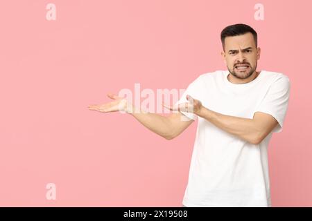 Gutaussehender, besorgter junger Mann, der etwas auf rosa Hintergrund zeigt Stockfoto